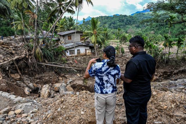Commuters stand near a landslide-affected area in the aftermath of Cyclone Ditwah, in Badulla on December 12, 2025. Two tropical storms dumped massive amounts of rain on the countries last month, prompting landslides and flooding that killed more than 600 people in Sri Lanka and nearly 1,000 in Indonesia. (Photo by Ishara S. KODIKARA / AFP)