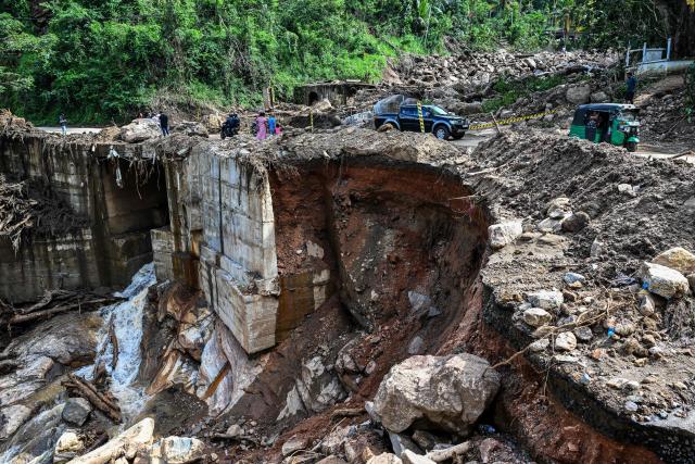 Commuters move through a damaged road along a landslide-affected area in the aftermath of Cyclone Ditwah, in Badulla on December 12, 2025. Two tropical storms dumped massive amounts of rain on the countries last month, prompting landslides and flooding that killed more than 600 people in Sri Lanka and nearly 1,000 in Indonesia. (Photo by Ishara S. KODIKARA / AFP)