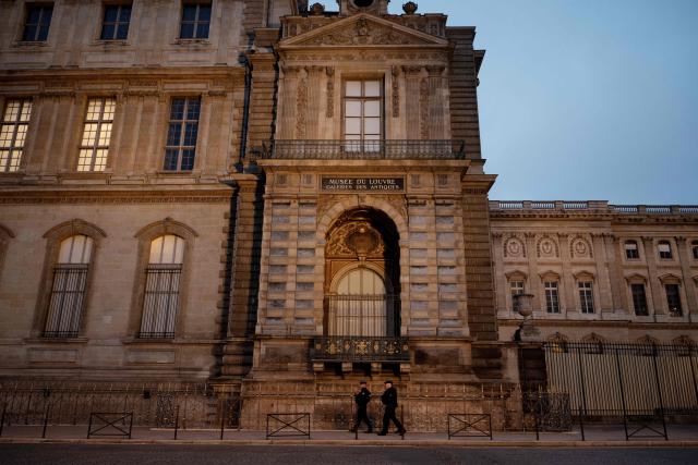 TOPSHOT - Police officers walk next to posts newly installed on the sidewalk along the Louvre Museum, on Quai Francois Mitterrand, in Paris on December 12, 2025, a few weeks after thieves used a furniture lift to break into the museum. Robbers broke into the Louvre and fled with jewellery on October 19, 2025 morning after arriving on a scooter armed with small chainsaws and used a goods lift to reach the room they were targeting. (Photo by Anna KURTH / AFP)