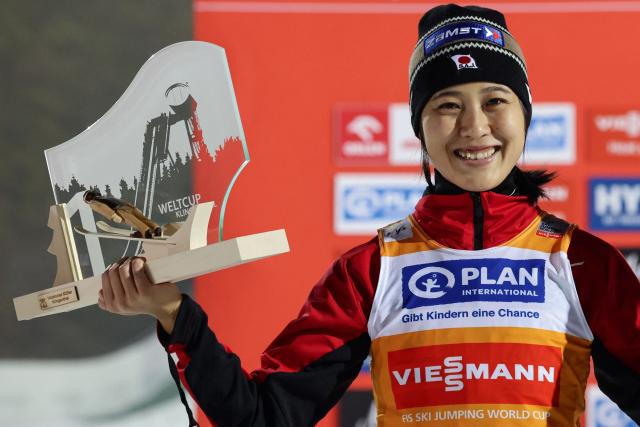 Japan's Nozomi Maruyama celebrates with the trophy on the podium after winning the women's Individual Large Hill HS140 event of the FIS Ski Jumping World Cup in Klingenthal, eastern Germany on December 12, 2025. Japan's Nozomi Maruyama won the event ahead of Slovenia's Nika Prevc (2nd) and Austria's Lisa Eder (3rd). (Photo by JENS SCHLUETER / AFP)