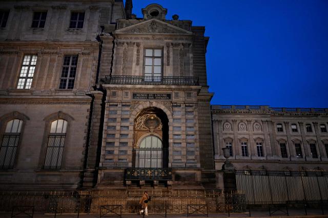 A woman walks next to posts newly installed on the sidewalk along the Louvre Museum, on Quai Francois Mitterrand, in Paris on December 12, 2025, a few weeks after thieves used a furniture lift to break into the museum. Robbers broke into the Louvre and fled with jewellery on October 19, 2025 morning after arriving on a scooter armed with small chainsaws and used a goods lift to reach the room they were targeting. (Photo by Anna KURTH / AFP)