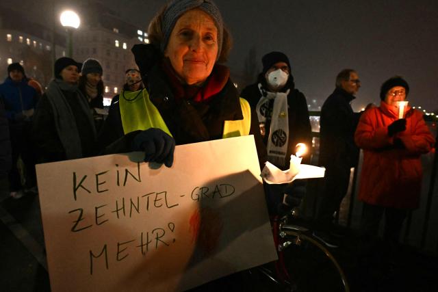 Environmental activists stage an action holding candles and a placard reading "Not a tenth of a degree further" to mark the 10th anniversary of the signing of the Paris Climate agreements, on December 12, 2025 in Vienna, Austria. (Photo by Joe Klamar / AFP)