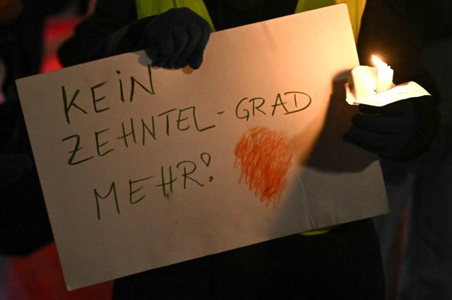 Environmental activists stage an actionholding a candle and a placard reading "Not a tenth of a degree further" to mark the 10th anniversary of the signing of the Paris Climate agreements, on December 12, 2025 in Vienna, Austria. (Photo by Joe Klamar / AFP)