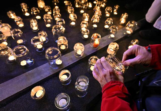 A protester lights candles on the sidelines of an action by Greenpeace environmental activists under the motto "Not a tenth of a degree further" to mark the 10th anniversary of the signing of the Paris Climate agreements, on December 12, 2025 in Vienna. (Photo by Joe Klamar / AFP)