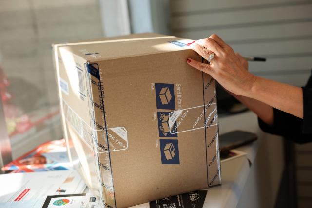 A customer writes an address on a package ahead of holiday shipping deadlines at the United States Postal Service (USPS) Gardena Post Office in Gardena, California, on December 12, 2025. The USPS reported an increase in expanded daily processing capacity from 60 million to 88 million packages nationwide by deploying more than 600 package sorters, with over 6 billion pieces of mail and packages accepted this holiday season. (Photo by Patrick T. Fallon / AFP)
