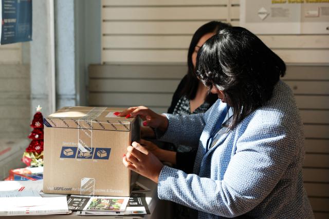 Postmaster Luwanda Smith helps customers with holiday shipping as they mail a package at the United States Postal Service (USPS) Gardena Post Office in Gardena, California, on December 12, 2025. The USPS reported an increase in expanded daily processing capacity from 60 million to 88 million packages nationwide by deploying more than 600 package sorters, with over 6 billion pieces of mail and packages accepted this holiday season. (Photo by Patrick T. Fallon / AFP)