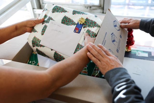 Customers pack a box with holiday gifts before mailing a package at the United States Postal Service (USPS) Gardena Post Office in Gardena, California, on December 12, 2025. The USPS reported an increase in expanded daily processing capacity from 60 million to 88 million packages nationwide by deploying more than 600 package sorters, with over 6 billion pieces of mail and packages accepted this holiday season. (Photo by Patrick T. Fallon / AFP)