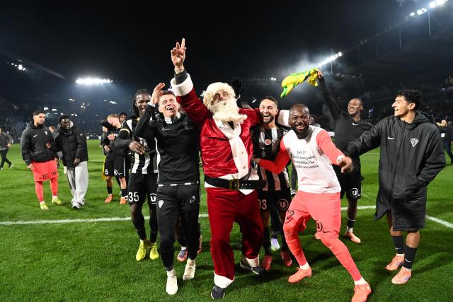 A man dressed as Santa Klaus is seen as Angers SCO players celebrate their victory at the end of the French L1 football match between SCO Angers and FC Nantes at the Raymond-Kopa Stadium in Angers, western France, on December 12, 2025. (Photo by JEAN-FRANCOIS MONIER / AFP)