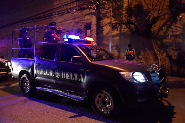 Bolivian police DELTA Special Action and Reaction Group officers patrol as they wait for the arrival of former Bolivian president Luis Arce (L) to the San Pedro Prison, after a judge ordered his preventive detention for five months while prosecutors investigate his alleged involvement in a corruption case, in La Paz on December 12, 2025. Arce, a 62-year-old economist, was arrested on December 10 after leaving office on November 8, ending a 20-year era of socialist governments initiated by indigenous leader Evo Morales. (Photo by Jorge BERNAL / AFP)