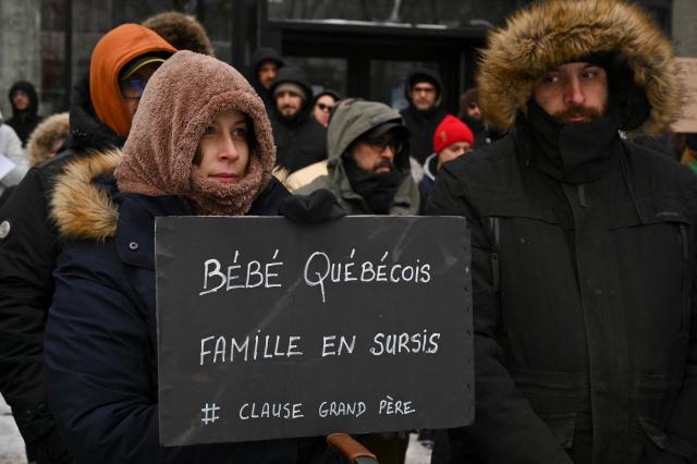 Pro immigration demonstrators hold a sign that reads in French: "Quebec baby, family on probation", as they protest in front of the Quebec Immigration Ministry in downtown Montreal, Canada, on December 12, 2025. Hundreds of protesters are calling on the Quebec government to allow immigrants already living in the province to stay, after the cancellation of a program that had allowed temporary workers to immigrate and obtain a pathway to permanent residency. (Photo by Daphné LEMELIN / AFP)