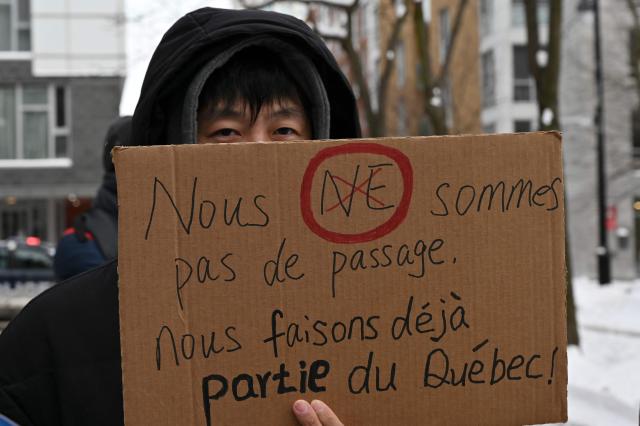 A pro immigration demonstrator holds a sign that reads in French: "We’re not just passing through, we’re already part of Quebec", as protesters gather in front of the Quebec Immigration Ministry in downtown Montreal, Canada, on December 12, 2025. Hundreds of protesters are calling on the Quebec government to allow immigrants already living in the province to stay, after the cancellation of a program that had allowed temporary workers to immigrate and obtain a pathway to permanent residency. (Photo by Daphnй LEMELIN / AFP)
