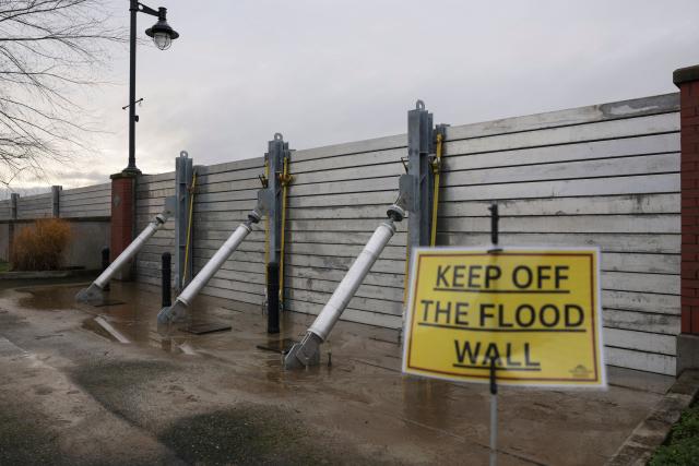 A warning sign is displayed in front of a flood wall along the Skagit River in Mount Vernon, Washington, on December 12, 2025. Tens of thousands of people were under evacuation orders on December 11 in western North America, after days of heavy rain forced rivers to burst their banks. Storms have battered Washington state in the US and British Columbia over the Canadian border for several days, with rivers continuing to rise. (Photo by Jason Redmond / AFP)
