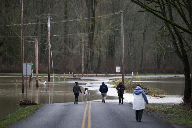 People watch the flood waters from the Skagit River at Riverfront Park in Sedro-Woolley, Washington, on December 12, 2025. Tens of thousands of people were under evacuation orders on December 11 in western North America, after days of heavy rain forced rivers to burst their banks. Storms have battered Washington state in the US and British Columbia over the Canadian border for several days, with rivers continuing to rise. (Photo by Jason Redmond / AFP)