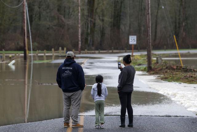 People watch the flood waters from the Skagit River at Riverfront Park in Sedro-Woolley, Washington, on December 12, 2025. Tens of thousands of people were under evacuation orders on December 11 in western North America, after days of heavy rain forced rivers to burst their banks. Storms have battered Washington state in the US and British Columbia over the Canadian border for several days, with rivers continuing to rise. (Photo by Jason Redmond / AFP)