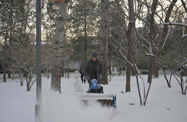 A worker clears snow in Ritan park one day after a heavy snowfall in Beijing on December 13, 2025. (Photo by Adek BERRY / AFP)