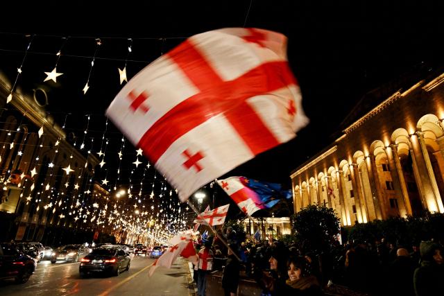 Demonstrators wave Georgian flags as they protest against the disputed parliamentary elections of 2024 in front of the parliament building in the street decorated with Christmas illuminations in Tbilisi on December 12, 2025. (Photo by Vano SHLAMOV / AFP)