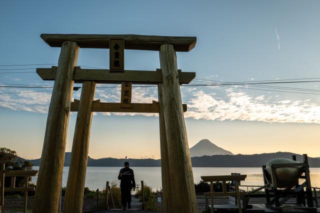 A man walks through the "Golden Torii" before Mount Kaimon (back) at lake Ikeda in Ibusuki, Kagoshima Prefecture on December 10, 2025. (Photo by Philip FONG / AFP)