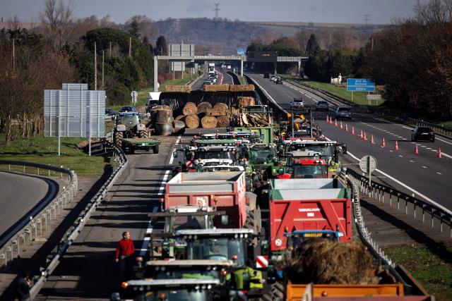 A wall of straw and tractors block access to the A64 motorway, in Carbonne, south-western France, on December 13, 2025. On December 12, 2025 French veterinarians slaughtered a herd of cows thought to be diseased after police dispersed angry farmers trying to protect them, an AFP reporter said, as an agricultural union called for nationwide protests. French farmers are unhappy with the state's management of an outbreak of nodular dermatitis -- widely known as lumpy skin disease. (Photo by Valentine CHAPUIS / AFP)