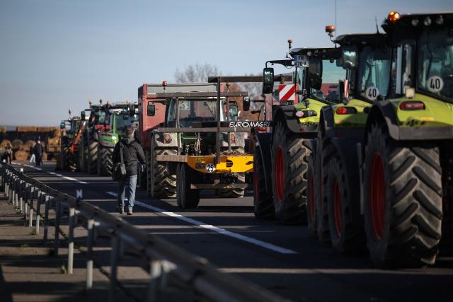 A man walks past tractors blocking the access to the A64 motorway, in Carbonne, south-western France, on December 13, 2025. On December 12, 2025 French veterinarians slaughtered a herd of cows thought to be diseased after police dispersed angry farmers trying to protect them, an AFP reporter said, as an agricultural union called for nationwide protests. French farmers are unhappy with the state's management of an outbreak of nodular dermatitis -- widely known as lumpy skin disease. (Photo by Valentine CHAPUIS / AFP)