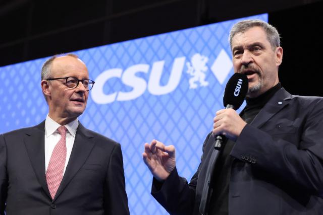 German Chancellor Friedrich Merz (L) and Bavaria's State Premier and leader of the conservative Christian Social Union (CSU) Markus Soeder are seen on stage during the congress of the Christian Social Union (CSU) party on December 13, 2025 in Munich, southern Germany. The Bavarian conservative Christian Social Union (CSU) party conference takes place on December 12 and 13, 2025 in the Fair Centre in Munich, southern Germany. (Photo by Alexandra BEIER / AFP)