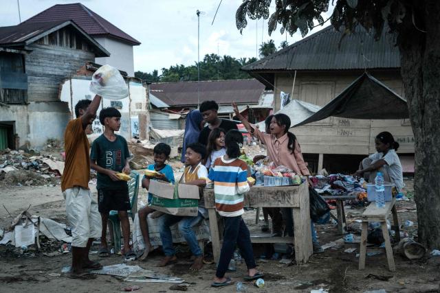 Children wait for donations in an area affected by a flash flood in the Aceh Tamiang, Northern Sumatra, on December 13, 2025. Devastating floods and landslides have killed 1,006 people in Indonesia, rescuers said December 13 as the Southeast Asian nation grapples with the huge scale of relief efforts. (Photo by Yasuyoshi CHIBA / AFP)
