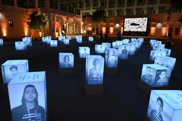 People attend an exhibition displaying portraits of 241 young victims of the war in Gaza at Msheireb Museums in Doha on December 13, 2025. The exhibition organised by Qatar Charity features 241 portraits of sponsored orphan children cared for through the compassion of donors, bringing their presence into a space where their names, faces and stories can be known and remembered. (Photo by Mahmud HAMS / AFP)