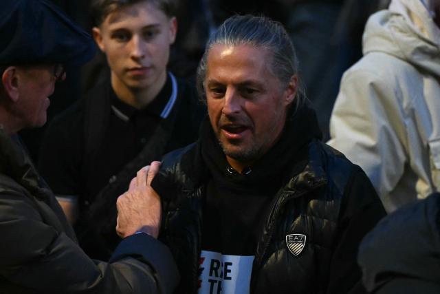 Co-founder of the Raise The Colours flag displaying movement, Ryan Bridge attends at an outdoor carol concert planned by British far-right activist Tommy Robinson, whose real name is Stephen Yaxley-Lennon, on Whitehall in central London on December 13, 2025. (Photo by JUSTIN TALLIS / AFP)