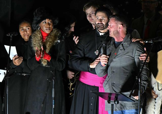 British far-right activist Tommy Robinson, whose real name is Stephen Yaxley-Lennon, reacts as he recieves a hug whist addressing supporters gathered to listen to him speak on stage, on Whitehall in central London on December 13, 2025, an outdoor carol concert event he organised. (Photo by JUSTIN TALLIS / AFP)