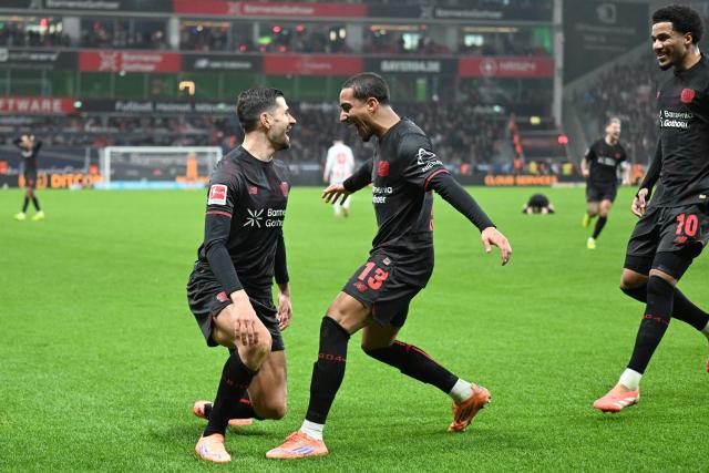 Bayer Leverkusen's French forward #11 Martin Terrier (L-R) celebrates scoring the opening goal with his teammates Bayer Leverkusen's Brazilian defender #13 Arthur and Bayer Leverkusen's US- German midfielder #10 Malik Tillman during the German first division Bundesliga football match between Bayer 04 Leverkusen and 1 FC Cologne in Leverkusen, western Germany, on December 13, 2025. (Photo by UWE KRAFT / AFP) / DFL REGULATIONS PROHIBIT ANY USE OF PHOTOGRAPHS AS IMAGE SEQUENCES AND/OR QUASI-VIDEO