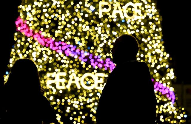 A couple stands by a Christmas tree bearing the word "peace" written in all the languages, is seen in Rome's City Hall Square Piazza del Capidoglio on December 13, 2025. (Photo by Filippo MONTEFORTE / AFP)