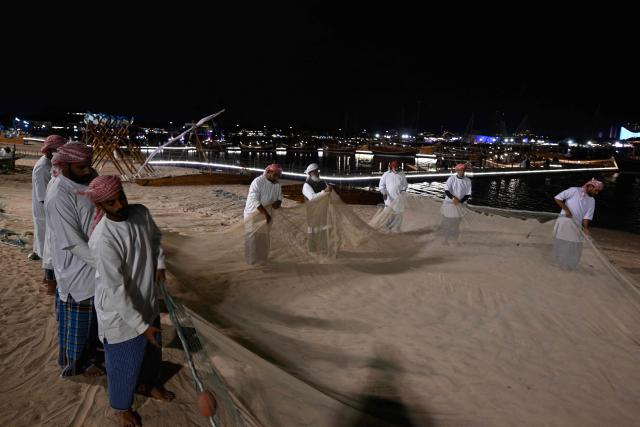Qatari fishermen prepare their fishing net at a waterfront in Doha on December 13, 2025. (Photo by Mahmud HAMS / AFP)