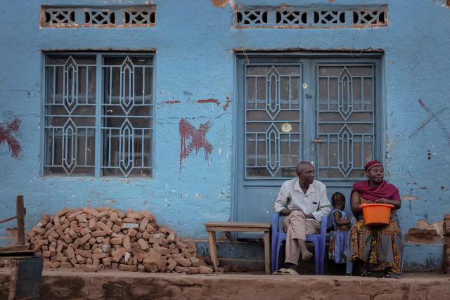 A family gathers at the doorway of their home in Uvira on December 13, 2025. The M23, backed by the Rwandan army, continued to advance on Saturday in eastern Democratic Republic of the Congo, despite Washington’s ire and its Saturday pledge to respond to Kigali’s “clear violation” of the peace agreement. After seizing the major cities of Goma in January and Bukavu in February, the M23 armed group launched a new offensive in early December in the eastern province of South Kivu, along the Burundian border, just as the DRC and Rwanda were signing a peace deal in Washington under the auspices of Donald Trump. On Wednesday, the armed group captured Uvira, a city of several hundred thousand inhabitants, enabling it to control the land border between the DRC and Burundi, a military backer of Kinshasa. (Photo by Jospin Mwisha / AFP)