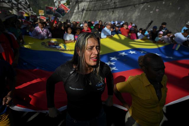 TOPSHOT - Supporters of Venezuelan President Nicolas Maduro display a giant Venezuelan flag as they take part in a rally against US military activity in the Caribbean, at the San Jose community in the Petare neighborhood in Caracas on December 13, 2025. Venezuelan President Nicolas Maduro on Thursday slammed the US seizure of an oil tanker from his country, calling it an act of "naval piracy" that escalated tensions between Washington and Caracas. (Photo by Federico PARRA / AFP)