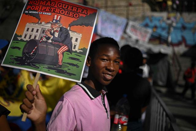 A supporter of Venezuelan President Nicolas Maduro shows a sign that reads in spanish "No more war for oil, the world demands it," as he takes part in a rally against US military activity in the Caribbean, at the San Jose community in the Petare neighborhood in Caracas on December 13, 2025. Venezuelan President Nicolas Maduro on Thursday slammed the US seizure of an oil tanker from his country, calling it an act of "naval piracy" that escalated tensions between Washington and Caracas. (Photo by Federico PARRA / AFP)