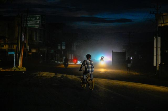 Motorists and cyclists ride down a dusty village road in an electrical blackout following devastating flash floods in Meureudu, Pidie Jaya district in Indonesia's Aceh province on December 13, 2025. Devastating floods and landslides have killed 1,006 people in Indonesia, rescuers said December 13 as the Southeast Asian nation grapples with the huge scale of relief efforts. (Photo by CHAIDEER MAHYUDDIN / AFP)