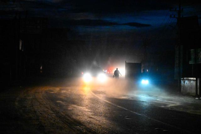 Motorists and a pedestrian are seen along a dusty village road in an electrical blackout following devastating flash floods in Meureudu, Pidie Jaya district in Indonesia's Aceh province on December 13, 2025. Devastating floods and landslides have killed 1,006 people in Indonesia, rescuers said December 13 as the Southeast Asian nation grapples with the huge scale of relief efforts. (Photo by CHAIDEER MAHYUDDIN / AFP)