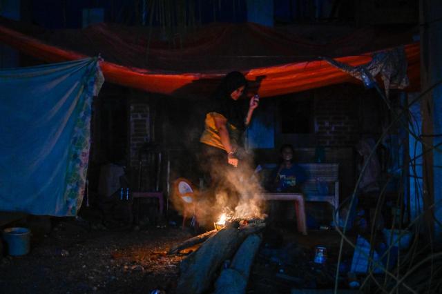 Flood-affected villagers gather by a fire during an electrical blackout following devastating flash floods in Meureudu, Pidie Jaya district in Indonesia's Aceh province on December 13, 2025. Devastating floods and landslides have killed 1,006 people in Indonesia, rescuers said December 13 as the Southeast Asian nation grapples with the huge scale of relief efforts. (Photo by CHAIDEER MAHYUDDIN / AFP)