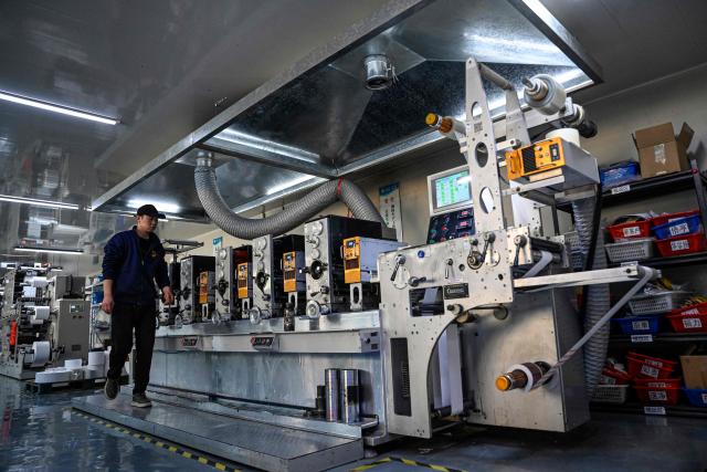 This photo taken on December 3, 2025 shows an employee working at a printing factory of Far East Precision Printing Company in Jiaxing, in eastern China's Zhejiang province. In a light-filled workshop in eastern China, a robotic arm moved a partially assembled autonomous vehicle as workers calibrated its cameras, typical of the incremental automation being adopted even across smaller factories in the world's manufacturing powerhouse. (Photo by Jade GAO / AFP) / To go with 'CHINA-ECONOMY-MANUFACTURING-TECHNOLOGY-AI, FOCUS' by Jing Xuan TENG