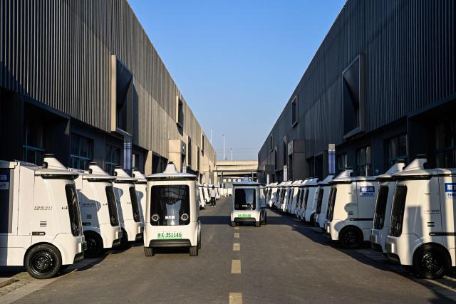This photo taken on December 4, 2025 shows Neolix X3 vehicles undergoing on-road testing at a factory of Chinese autonomous delivery vehicle maker Neolix in Yancheng, in eastern China's Jiangsu province. In a light-filled workshop in eastern China, a robotic arm moved a partially assembled autonomous vehicle as workers calibrated its cameras, typical of the incremental automation being adopted even across smaller factories in the world's manufacturing powerhouse. (Photo by Jade GAO / AFP) / To go with 'CHINA-ECONOMY-MANUFACTURING-TECHNOLOGY-AI, FOCUS' by Jing Xuan TENG