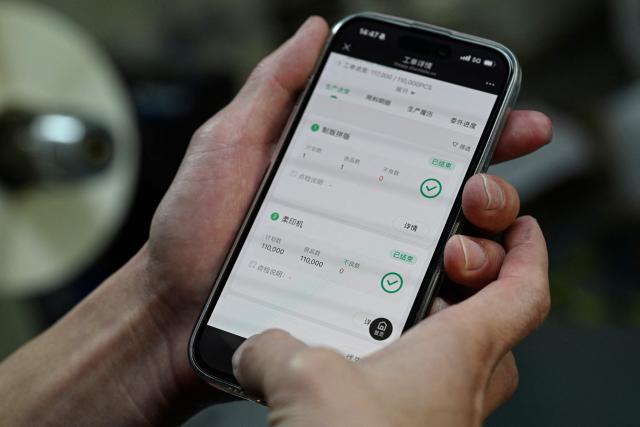 This photo taken on December 3, 2025 shows an employee uploading product data via the Blacklake platform at a printing factory of Far East Precision Printing Company in Jiaxing, in eastern China's Zhejiang province. In a light-filled workshop in eastern China, a robotic arm moved a partially assembled autonomous vehicle as workers calibrated its cameras, typical of the incremental automation being adopted even across smaller factories in the world's manufacturing powerhouse. (Photo by Jade GAO / AFP) / To go with 'CHINA-ECONOMY-MANUFACTURING-TECHNOLOGY-AI, FOCUS' by Jing Xuan TENG