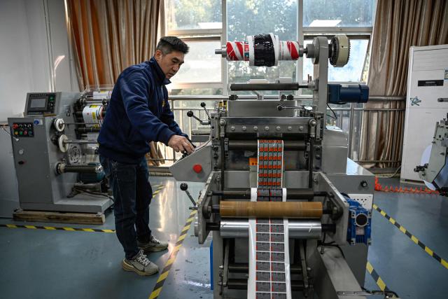 This photo taken on December 3, 2025 shows an employee working at a printing factory of Far East Precision Printing Company in Jiaxing, in eastern China's Zhejiang province. In a light-filled workshop in eastern China, a robotic arm moved a partially assembled autonomous vehicle as workers calibrated its cameras, typical of the incremental automation being adopted even across smaller factories in the world's manufacturing powerhouse. (Photo by Jade GAO / AFP) / To go with 'CHINA-ECONOMY-MANUFACTURING-TECHNOLOGY-AI, FOCUS' by Jing Xuan TENG