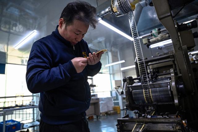 This photo taken on December 3, 2025 shows an employee checking products at a printing factory of Far East Precision Printing Company in Jiaxing, in eastern China's Zhejiang province. In a light-filled workshop in eastern China, a robotic arm moved a partially assembled autonomous vehicle as workers calibrated its cameras, typical of the incremental automation being adopted even across smaller factories in the world's manufacturing powerhouse. (Photo by Jade GAO / AFP) / To go with 'CHINA-ECONOMY-MANUFACTURING-TECHNOLOGY-AI, FOCUS' by Jing Xuan TENG