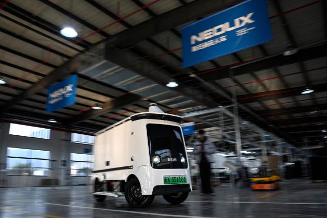 This photo taken on December 4, 2025 shows a Neolix X3 vehicle rolling off the production line at a factory of Chinese autonomous delivery vehicle maker Neolix in Yancheng, in eastern China's Jiangsu province. In a light-filled workshop in eastern China, a robotic arm moved a partially assembled autonomous vehicle as workers calibrated its cameras, typical of the incremental automation being adopted even across smaller factories in the world's manufacturing powerhouse. (Photo by Jade GAO / AFP) / To go with 'CHINA-ECONOMY-MANUFACTURING-TECHNOLOGY-AI, FOCUS' by Jing Xuan TENG