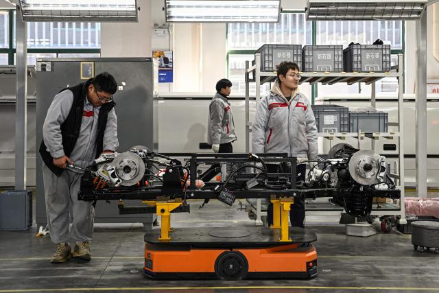 This photo taken on December 4, 2025 shows employees working on a Neolix X3 vehicle production line at a factory of Chinese autonomous delivery vehicle maker Neolix in Yancheng, in eastern China's Jiangsu province. In a light-filled workshop in eastern China, a robotic arm moved a partially assembled autonomous vehicle as workers calibrated its cameras, typical of the incremental automation being adopted even across smaller factories in the world's manufacturing powerhouse. (Photo by Jade GAO / AFP) / To go with 'CHINA-ECONOMY-MANUFACTURING-TECHNOLOGY-AI, FOCUS' by Jing Xuan TENG