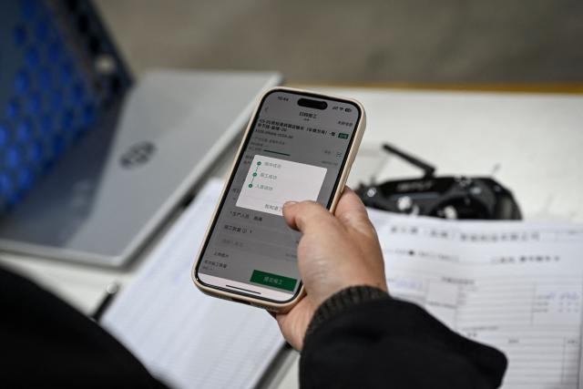 This photo taken on December 4, 2025 shows an employee uploading product data via the Blacklake platform at a factory of Chinese autonomous delivery vehicle maker Neolix in Yancheng, in eastern China's Jiangsu province. In a light-filled workshop in eastern China, a robotic arm moved a partially assembled autonomous vehicle as workers calibrated its cameras, typical of the incremental automation being adopted even across smaller factories in the world's manufacturing powerhouse. (Photo by Jade GAO / AFP) / To go with 'CHINA-ECONOMY-MANUFACTURING-TECHNOLOGY-AI, FOCUS' by Jing Xuan TENG