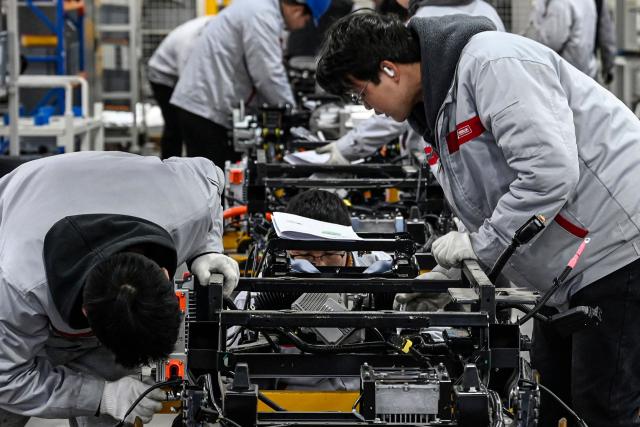 This photo taken on December 4, 2025 shows employees working on a Neolix X3 vehicle production line at a factory of Chinese autonomous delivery vehicle maker Neolix in Yancheng, in eastern China's Jiangsu province. In a light-filled workshop in eastern China, a robotic arm moved a partially assembled autonomous vehicle as workers calibrated its cameras, typical of the incremental automation being adopted even across smaller factories in the world's manufacturing powerhouse. (Photo by Jade GAO / AFP) / To go with 'CHINA-ECONOMY-MANUFACTURING-TECHNOLOGY-AI, FOCUS' by Jing Xuan TENG