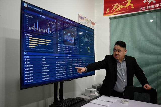 This photo taken on December 3, 2025 shows Zhu Yefeng, General Manager of Far East Precision Printing Company showing the screen monitoring production lines at a printing factory in Jiaxing, in eastern China's Zhejiang province. In a light-filled workshop in eastern China, a robotic arm moved a partially assembled autonomous vehicle as workers calibrated its cameras, typical of the incremental automation being adopted even across smaller factories in the world's manufacturing powerhouse. (Photo by Jade GAO / AFP) / To go with 'CHINA-ECONOMY-MANUFACTURING-TECHNOLOGY-AI, FOCUS' by Jing Xuan TENG