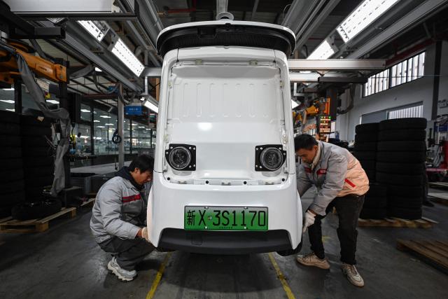 This photo taken on December 4, 2025 shows employees working on a Neolix X3 vehicle production line at a factory of Chinese autonomous delivery vehicle maker Neolix in Yancheng, in eastern China's Jiangsu province. In a light-filled workshop in eastern China, a robotic arm moved a partially assembled autonomous vehicle as workers calibrated its cameras, typical of the incremental automation being adopted even across smaller factories in the world's manufacturing powerhouse. (Photo by Jade GAO / AFP) / To go with 'CHINA-ECONOMY-MANUFACTURING-TECHNOLOGY-AI, FOCUS' by Jing Xuan TENG