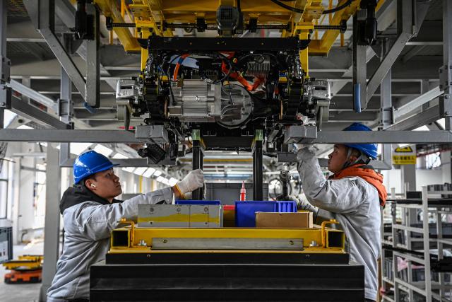 This photo taken on December 4, 2025 shows employees working on a Neolix X3 vehicle production line at a factory of Chinese autonomous delivery vehicle maker Neolix in Yancheng, in eastern China's Jiangsu province. In a light-filled workshop in eastern China, a robotic arm moved a partially assembled autonomous vehicle as workers calibrated its cameras, typical of the incremental automation being adopted even across smaller factories in the world's manufacturing powerhouse. (Photo by Jade GAO / AFP) / To go with 'CHINA-ECONOMY-MANUFACTURING-TECHNOLOGY-AI, FOCUS' by Jing Xuan TENG