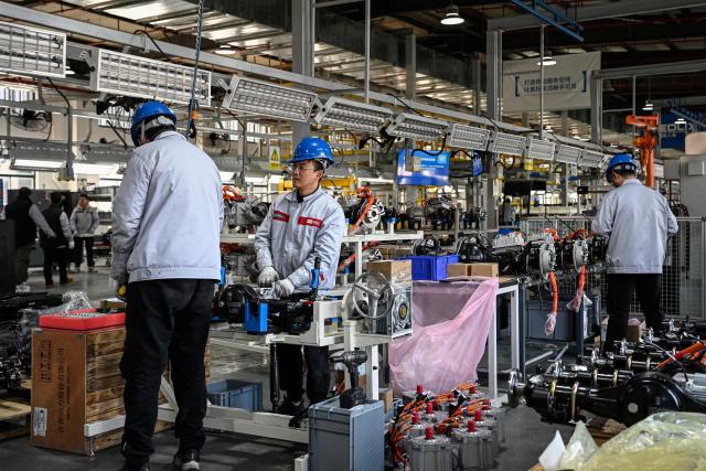 This photo taken on December 4, 2025 shows employees working on a Neolix X3 vehicle production line at a factory of Chinese autonomous delivery vehicle maker Neolix in Yancheng, in eastern China's Jiangsu province. In a light-filled workshop in eastern China, a robotic arm moved a partially assembled autonomous vehicle as workers calibrated its cameras, typical of the incremental automation being adopted even across smaller factories in the world's manufacturing powerhouse. (Photo by Jade GAO / AFP) / To go with 'CHINA-ECONOMY-MANUFACTURING-TECHNOLOGY-AI, FOCUS' by Jing Xuan TENG